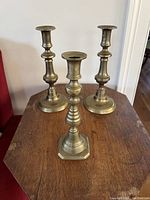Photo of three vintage brass candlesticks, two matching with smooth classic shapes and one single ribbed design candlestick in front.