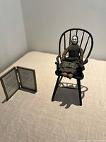 China head doll seated in miniature Windsor doll chair with framed historic documents on table
