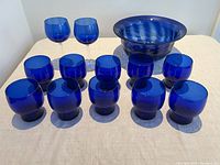 Full collection showing all 13 pieces: 2 cobalt blue wine glasses with clear stems, 10 cobalt blue beehive tumblers, 1 cobalt blue hand-blown bowl.