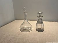 Pair of glass decanters on beige surface against white background, showing shape and stopper styles.