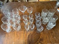 Wide top-down view of all clear glassware including high balls, low balls, beer, and wine glasses arranged on a wooden table.