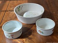Photo of all three soufflé dishes together on wood surface showing two smaller dishes with decorative motifs and larger dish with crack