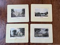 Four Lady Clare placemats laid out on a wooden surface showing their vintage illustration prints of British landscapes, including Windsor Castle and Cambridge University.