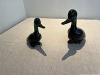 Pair of green and black Murano glass ducks side by side on beige cloth surface showing overall size and color