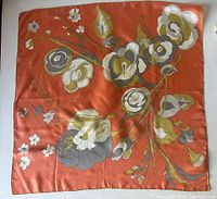 Flat lay of the full silk scarf showing floral design in peachy orange, grey, ecru, and olive tones