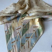 Silk scarf spread out on a flat surface showing the cream background with brown circular dots and the geometric pattern border with muted color triangles and lines.
