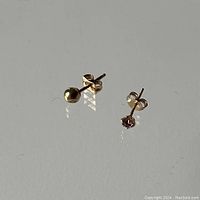 Photo showing two 10K gold stud earrings: a gold ball stud with a visible ding and a pink stone stud.