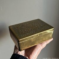Box held in hand showing size and exterior brass body with subtle patina and Art Deco engraving on lid