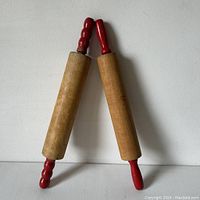 Two wooden rolling pins with red painted handles positioned against a white background.