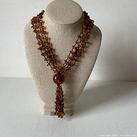 Front view of the cognac amber multi-strand necklace on a bust showing the tassel and overall structure.