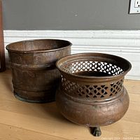 Image showing both copper planter pots side by side on wood floor against wall.