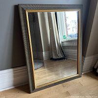 View of full gold toned framed mirror angled against wall showing reflection and frame condition.