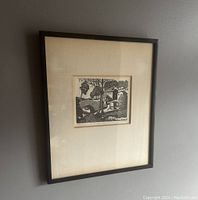 Framed black and white block print depicting a rural scene with a stone bridge, trees, houses, and a wayside shrine.
