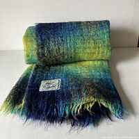 Folded throw showing tartan pattern in cobalt blue, lime green, and turquoise, with fringed edges and sewn label.