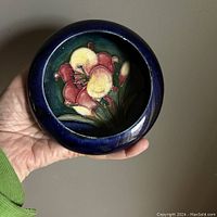 Top view showing floral design inside shallow cobalt blue dish held in hand.