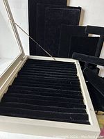 Open white display box showing black velvet ring rolls inside and multiple black velvet display boards behind it.