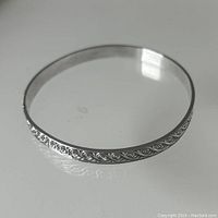 Photo showing the full bangle with surface pattern and overall shape on a reflective white surface.