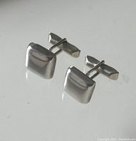 Pair of squared sterling silver cufflinks with polished finish displayed on reflective surface, showing front and side views.