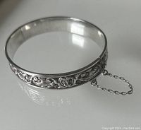 Front and angled view showing the embossed floral and scroll pattern with attached safety chain.