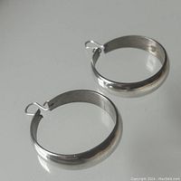 Pair of smooth polished sterling silver hoop earrings laid flat showing rounded shape and ear hanger hooks.