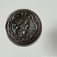 Top view showing the hinged lid with raised religious figure and decorative motifs around the edge.