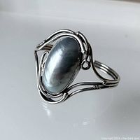 Full view of sterling silver handmade cuff bracelet with large oval mabe pearl, showing reflective pearl and silver wire design.
