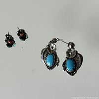 Pair of two distinct Navajo sterling silver earrings on a white background, larger turquoise ones with floral leaf design and smaller turquoise-red coral cluster earrings.