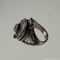 Side angle showing filigree detail and green stone on hinged poison ring