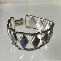 Close-up photo of sterling silver bracelet with sodalite inset diamond-shaped links shown on reflective surface.
