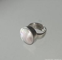 Front perspective of sterling silver ring with polished round mother of pearl inset showing color and texture.