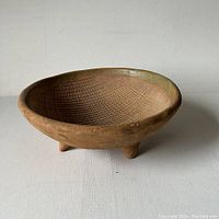 Vintage brown clay bowl with textured crosshatch pattern inside, round with slightly flared rim and supported by three short triangular feet, on a plain white surface.