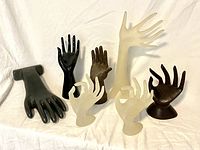 Seven assorted vintage display hands in resin and metal arranged on white fabric background showing various hand gestures and colors.