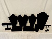 Front view of all black velvet jewelry display pieces arranged on a white backdrop including necklace busts, ring trays, bracelet T-bars, flat displays, and earring stands with earrings.
