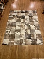 Full view of patchwork cowhide rug laid flat on wood floor shows its overall size, color pattern and condition.