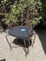 Front angle view showing the iron scroll design on back and armrests, black cushion attached to seat.