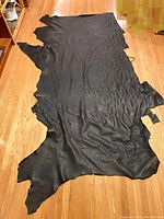 Full view of dark brown leather hyde spread on wooden floor showing size and shape.