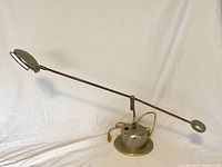 Full view of lamp showing weighted base and long adjustable arm with counterweight and round lamp head.