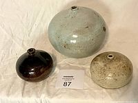 Three vintage pottery weedpots arranged together on cloth with auction bid card.