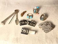 Full collection of vintage jewelry items including cufflinks, tie clip, rings, brooch, pendant, and pipe cleaner tool arranged on beige fabric.