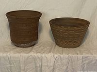 Two stoneware planter pots, one taller cylindrical with horizontal textured bands and white residue near the base, and one shorter wider with similar patterned bands.