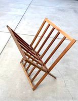 View of wooden artist print rack angled slightly to show front slatted design and foldable A-frame construction on concrete.