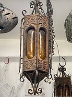 Front view of one large wooden and iron chandelier featuring carved floral wood panels and two amber glass inserts held by iron chains.