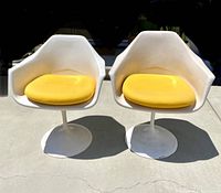 Front view of the two white tulip chairs with yellow cushions placed side by side on concrete surface.