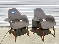 Front view of paired upholstered chairs with wooden legs in light brown fabric upholstery.