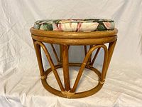 Front side view of the bamboo cane ottoman with floral cushion on top.