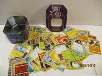 Photo showing the full spread of the 110+ Pokemon trading cards in various types and conditions next to the collectible metal tin.