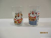 Two clear glasses with colorful Tony the Tiger graphics from Kellogg's Frosted Flakes cereal.