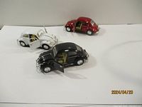 Three Kinsmart 1967 Volkswagen Beetles in red, white, and black with doors open and detail visible