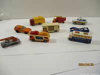 Nine vintage Matchbox toy vehicles arranged on a white surface showing various types of vehicles including trucks, campers, sports cars, and emergency vehicles.