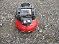 Front and top view of red Porter Cable air compressor on gravel ground showing control panel and brand name.